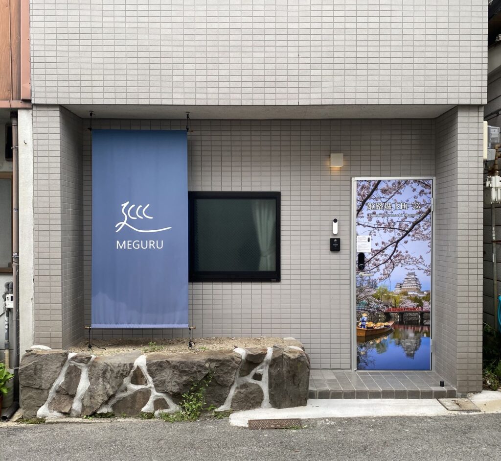 姫路城下町 巡の外観。藍色の暖簾と、姫路城を描いた扉のアート